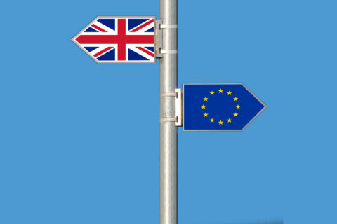 Zu sehen sind Wegweiser, wobei einer die birtische und einer die Flagge der EU zeigt. Sie zeigen in entgegengesetzte Richtungen.